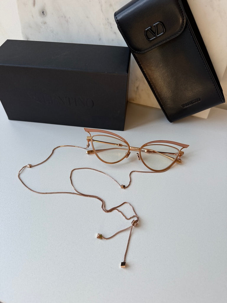 Gold-tone cat-eye eyeglass frames with beige lenses and long chain necklace