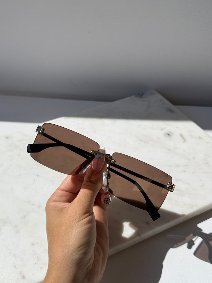 Rimless sunglasses side view with brown lenses, gold hinges, black temple arms