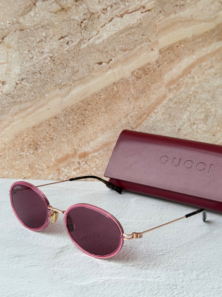 Gucci oval pink sunglasses with dark lenses, thin gold arms, and pink case