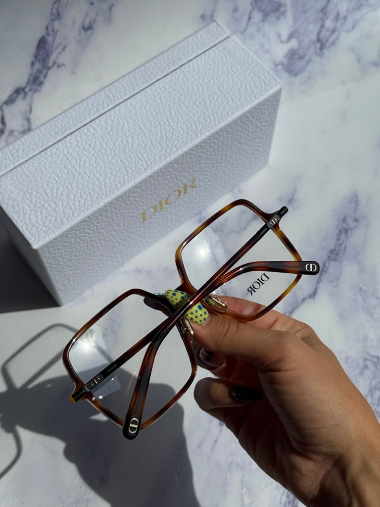 Havana brown square eyeglasses held in hand near white Dior gift box