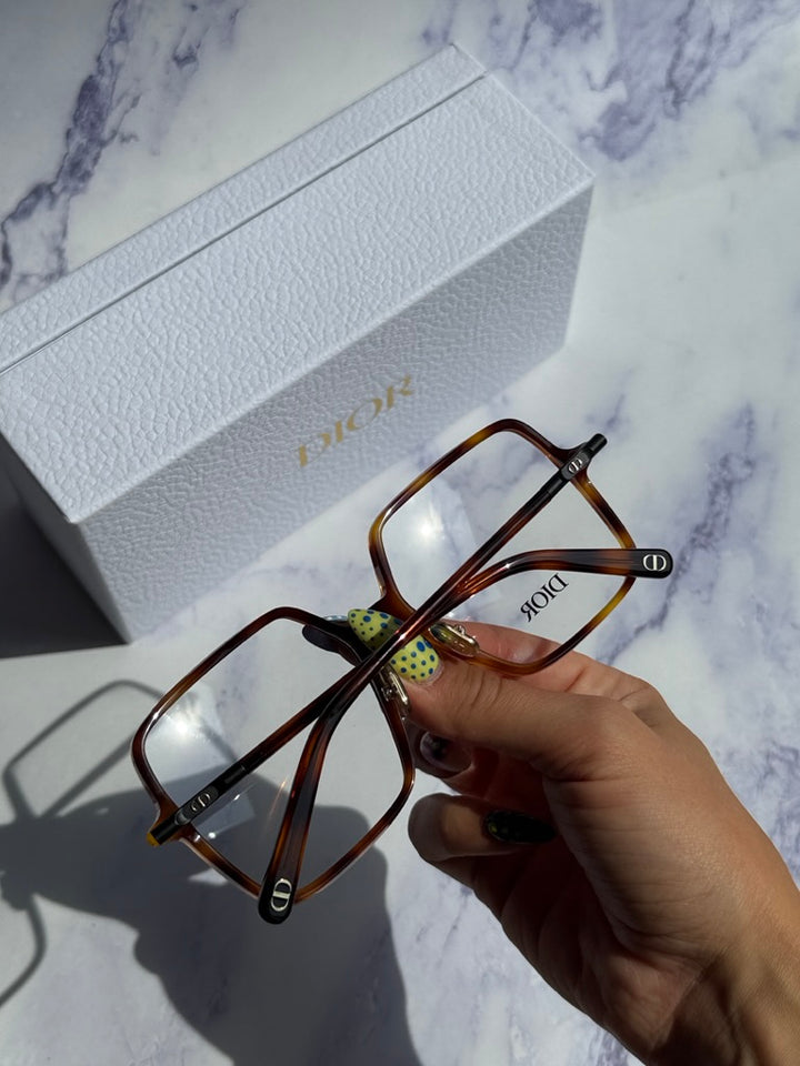 Havana brown square eyeglasses held in hand near white Dior gift box