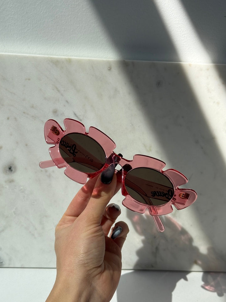 Loewe pink flower sunglasses held up, dark lenses and logo on the temples