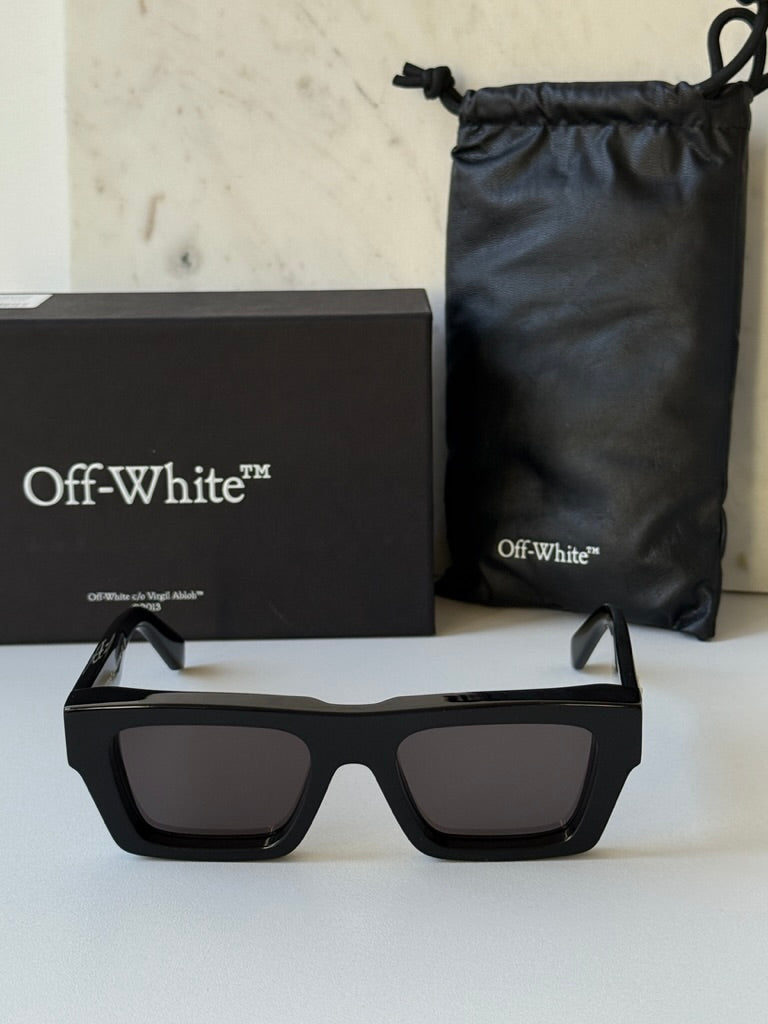 Black oversized sunglasses with dark lenses and Off-White temple logo, beside pouch and box