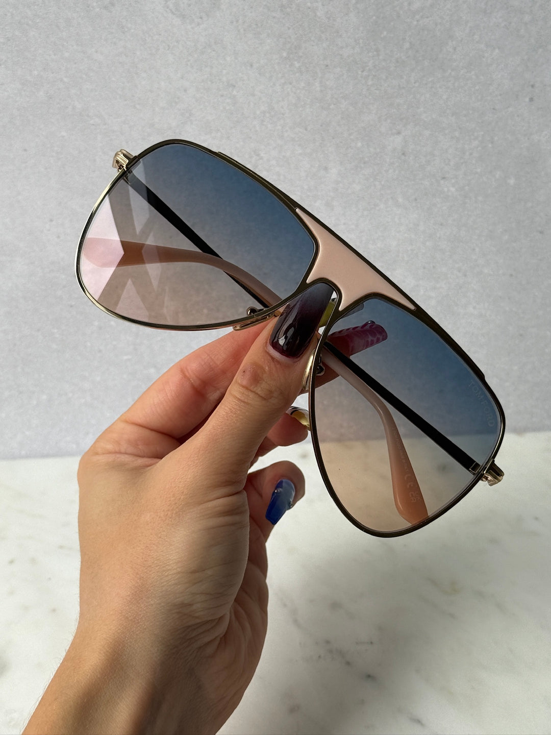 Aviator sunglasses with blue gradient lenses and gold frame, held in hand