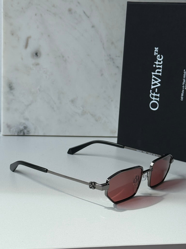 Loa sunglasses on side, burgundy lenses with gunmetal frame beside Off White case