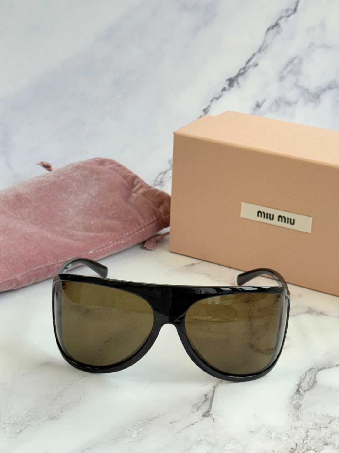 Oversized black shield sunglasses with brown gradient lenses and a pink cloth pouch.