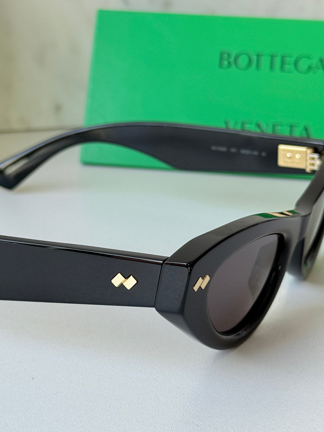 Black cat-eye sunglasses close-up with gold-tone emblem on temple and dark lenses.