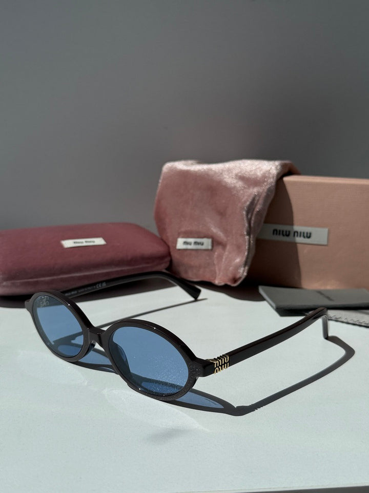 Oval dark brown sunglasses with blue lenses, laid out with accessories