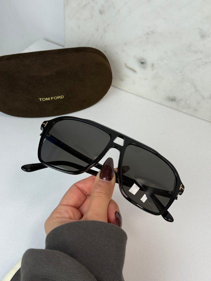 Black Tom Ford sunglasses with dark lenses and gold-tone accents; case shown.