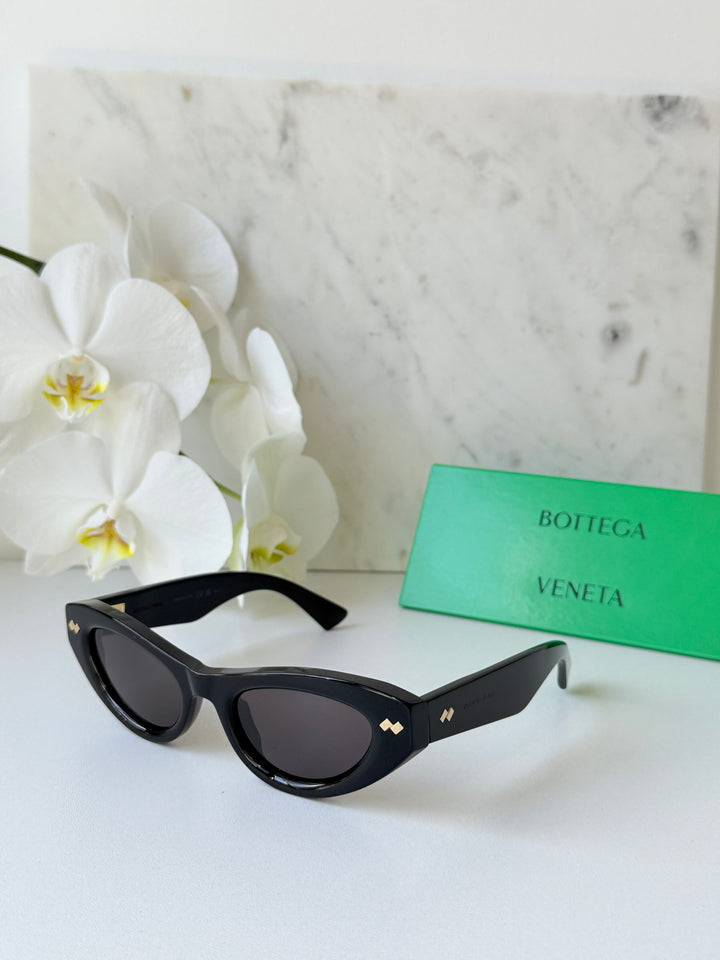 Black cat-eye sunglasses with dark lenses, curved silhouette, gold-tone logo detail.