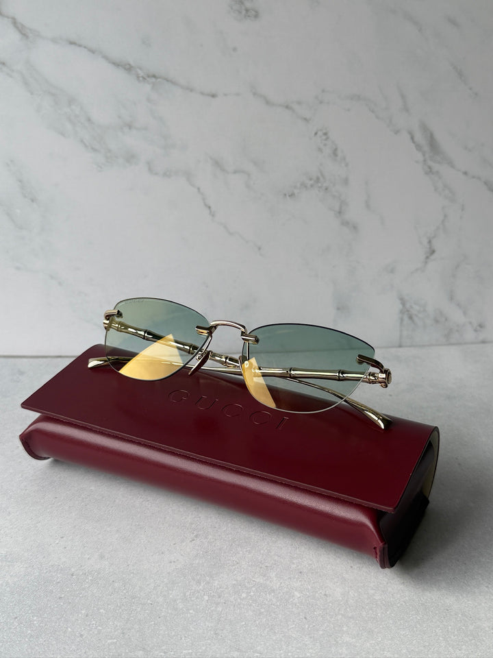 Cat-eye sunglasses with green lenses, gold-tone frame, resting on a burgundy case