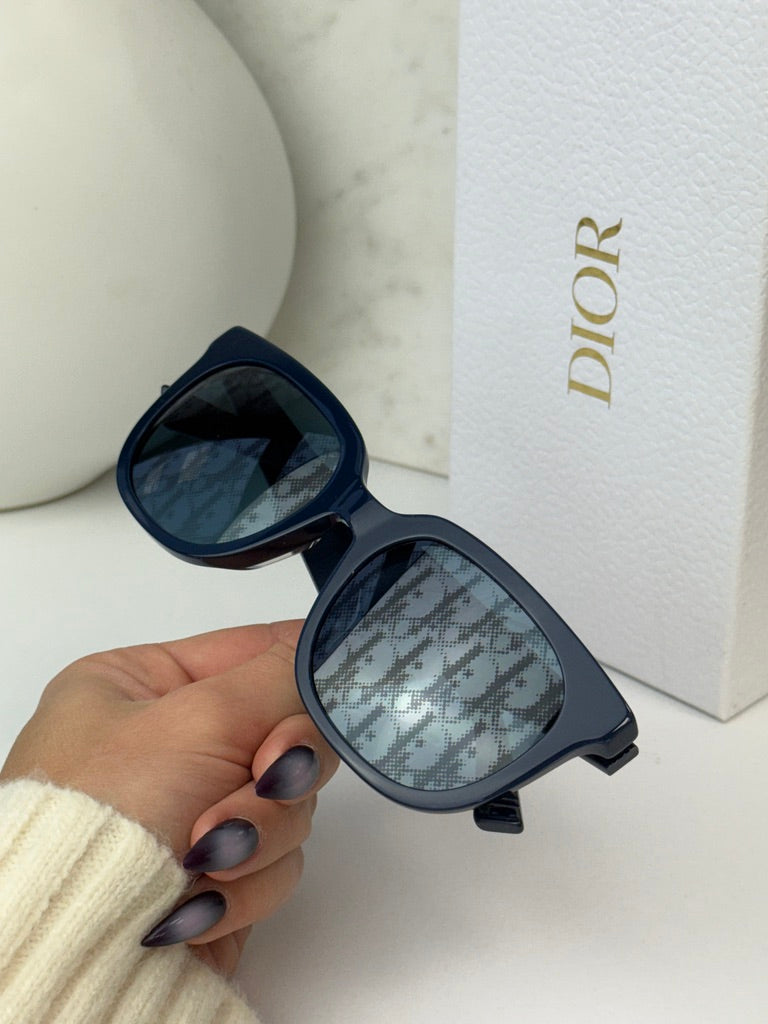 Navy Dior sunglasses with dark mirror lenses and logo temple detail, held in hand.