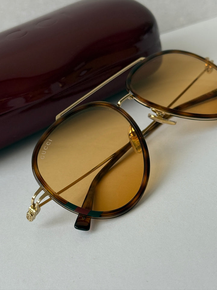 Gucci aviator sunglasses close-up, brown frame with gold hinges and amber tinted lenses