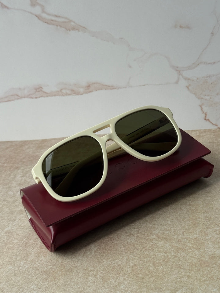 GUCCI aviator sunglasses, ivory frames with dark lenses, side view on burgundy case