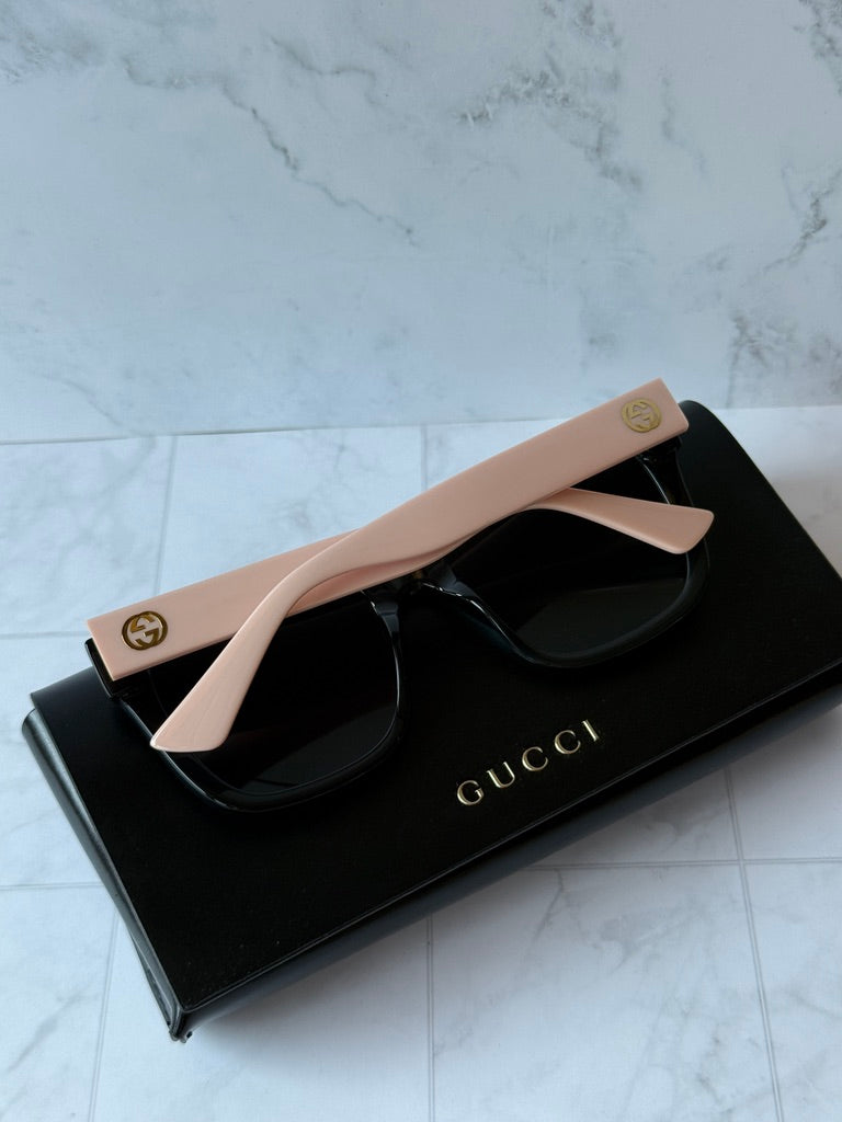 Sunglasses with black frames, pink temples, and dark lenses; Gucci logo on arms