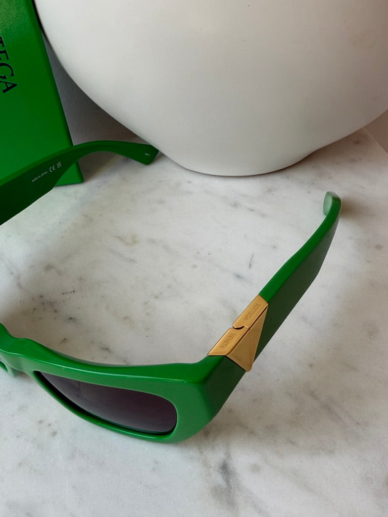 Green cat-eye sunglasses side close-up with gold-tone logo plate and temple