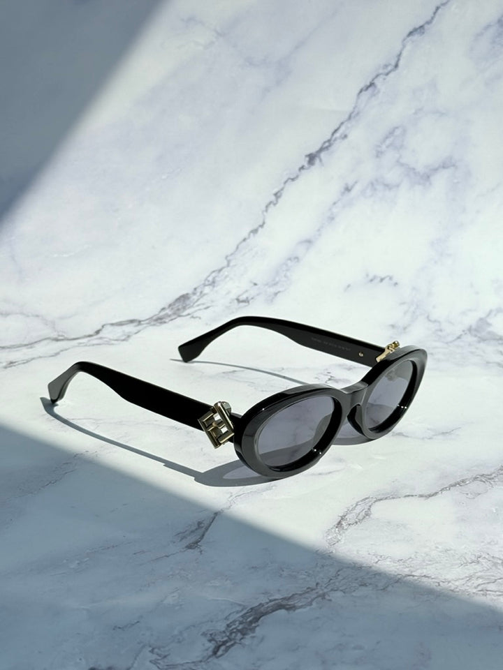 Black oval sunglasses with dark lenses and gold logo hinge, side view