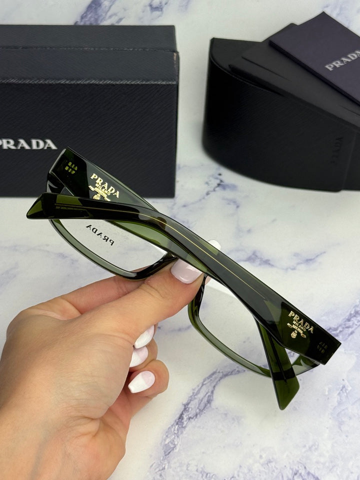Transparent green eyeglass frames, close temple view with Prada text and hinge detail.