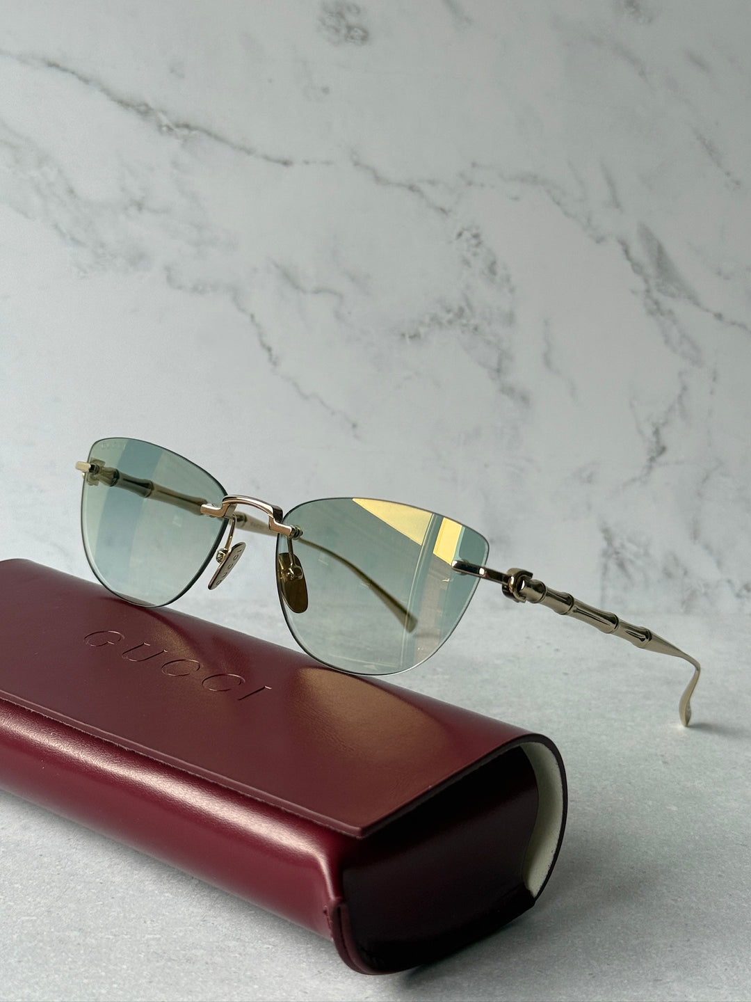 Gold-tone cat-eye sunglasses with green lenses on a burgundy case, side view