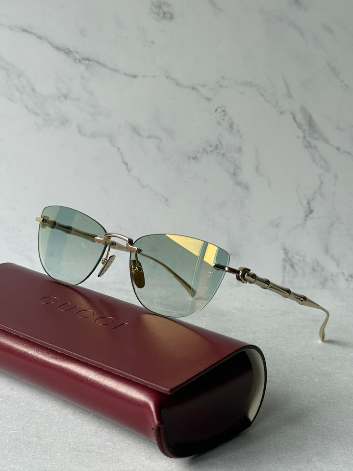 Gold-tone cat-eye sunglasses with green lenses on a burgundy case, side view