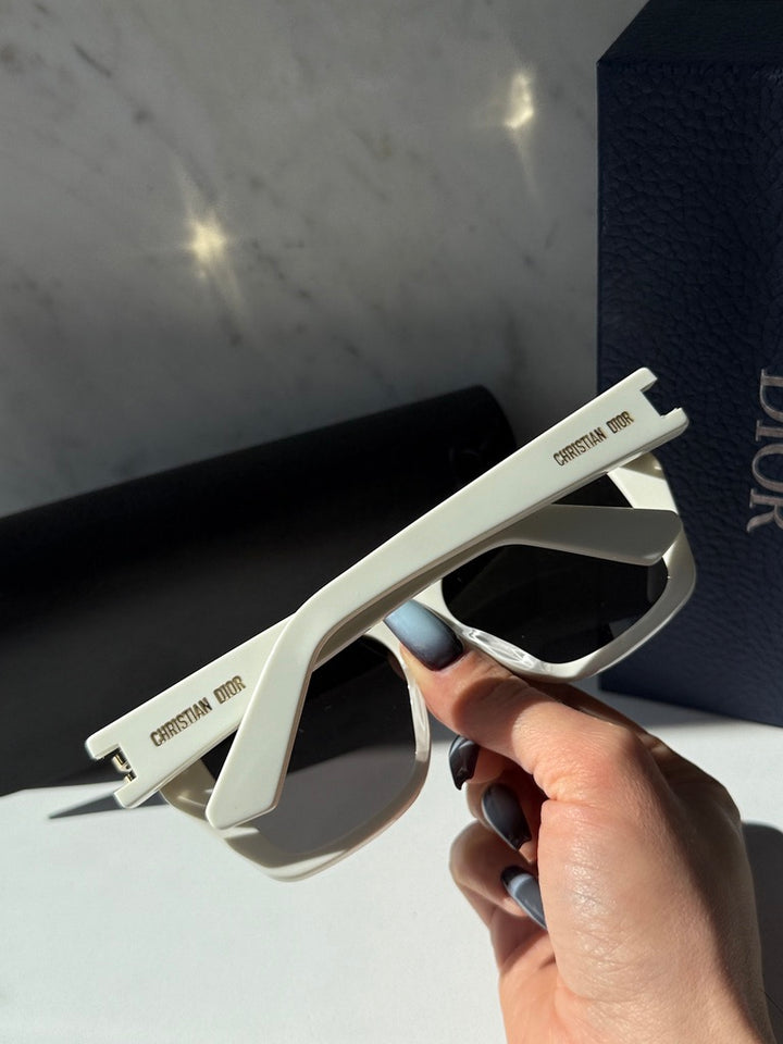 Oversized butterfly sunglasses close-up: white frame, dark lenses, gold logo on temple