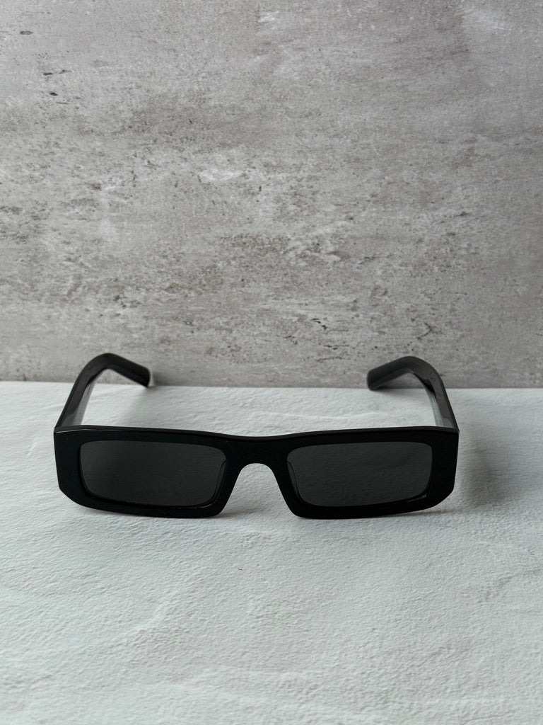 Prada black rectangular sunglasses with dark lenses, front view on a surface.