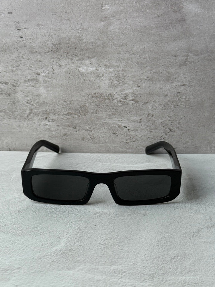 Prada black rectangular sunglasses with dark lenses, front view on a surface.