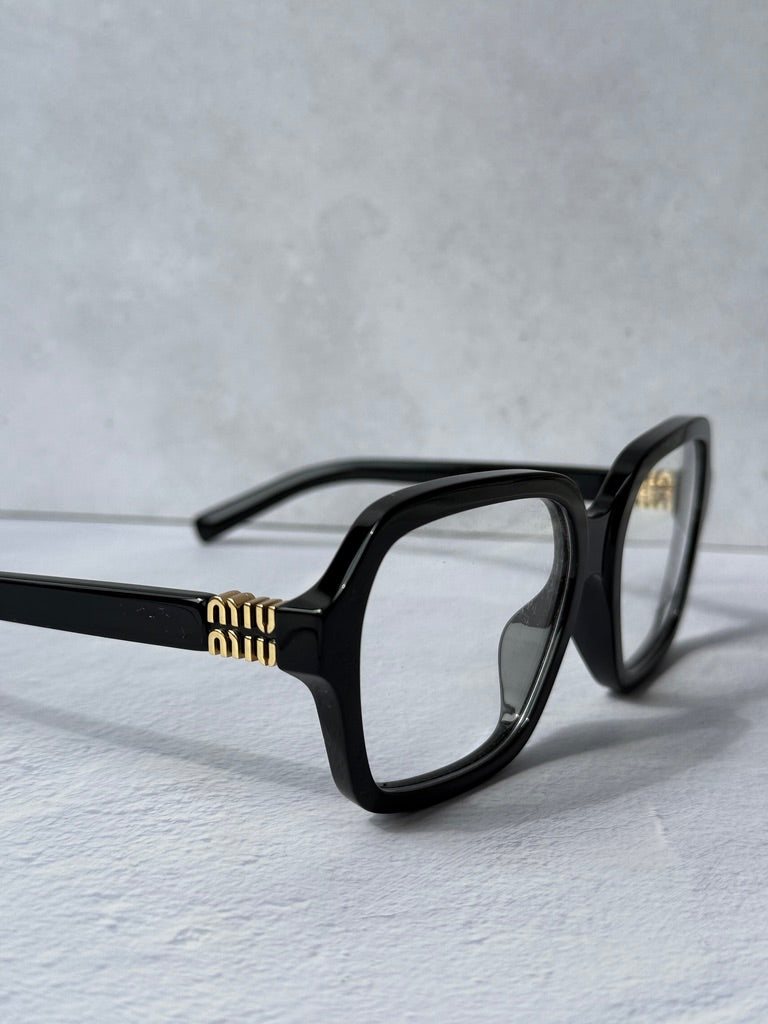 Black square eyeglass frames with gold logo on temple, angled side view