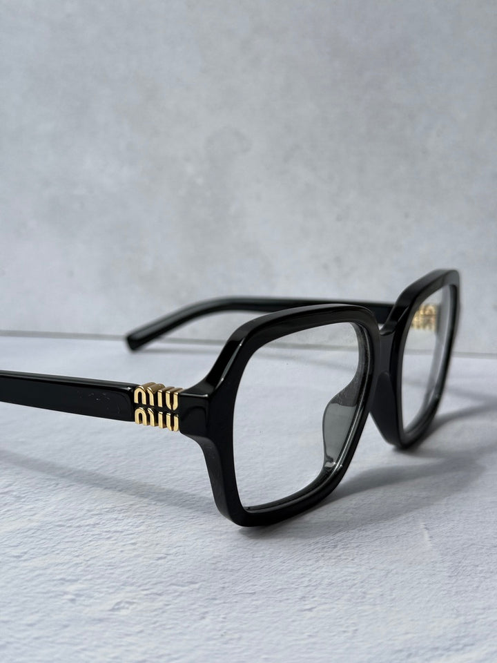 Black square eyeglass frames with gold logo on temple, angled side view