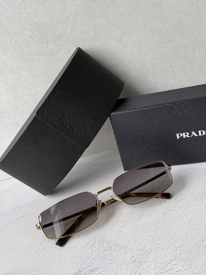 Gold metal rectangle sunglasses with gray tinted lenses and PRADA branding on case