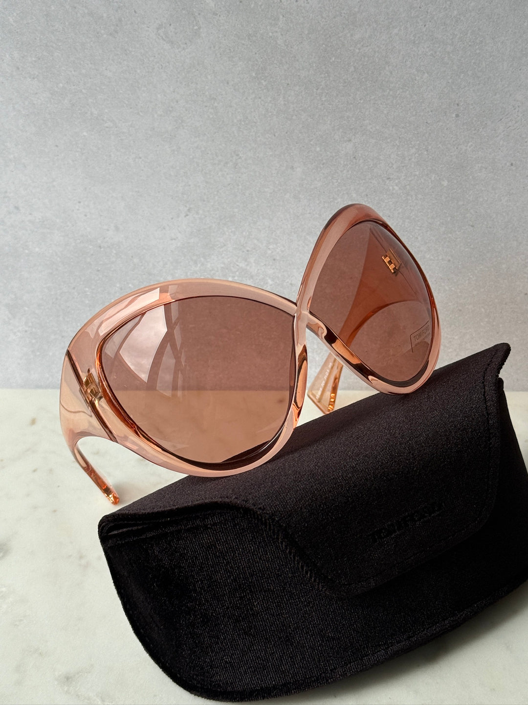 Oversized mask sunglasses, pink frame and brown lenses, resting on black eyeglass pouch.