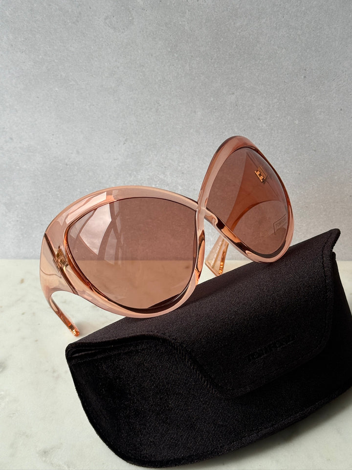 Oversized mask sunglasses, pink frame and brown lenses, resting on black eyeglass pouch.
