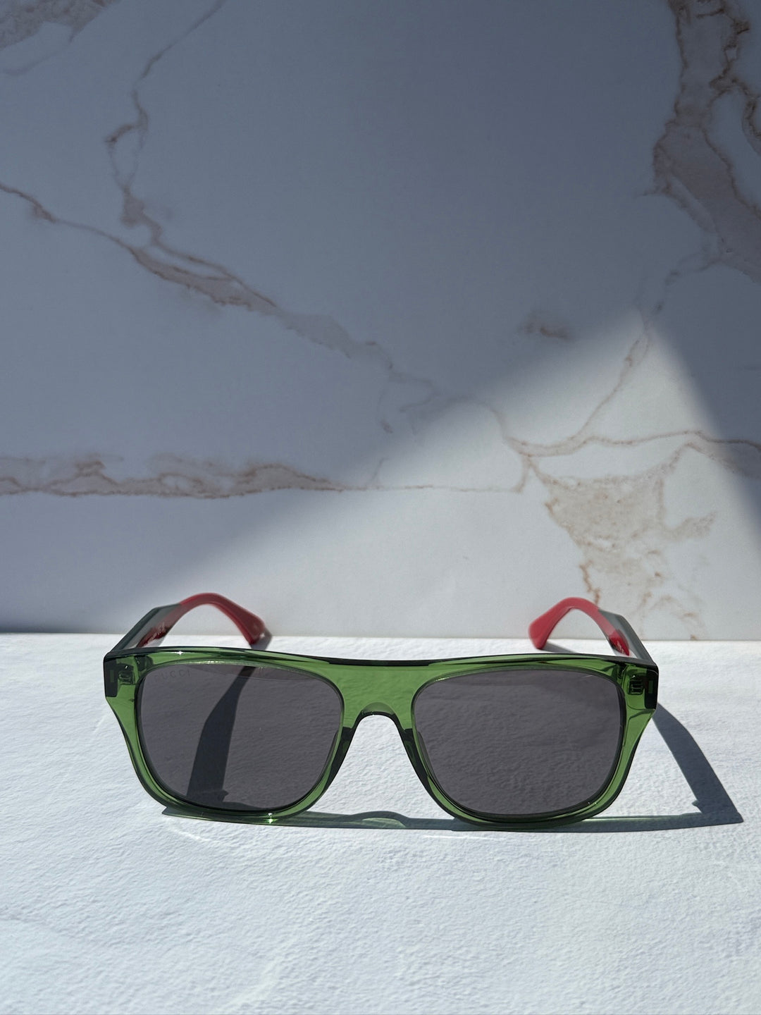 Gucci striped green sunglasses with dark lenses, red tips on temples.