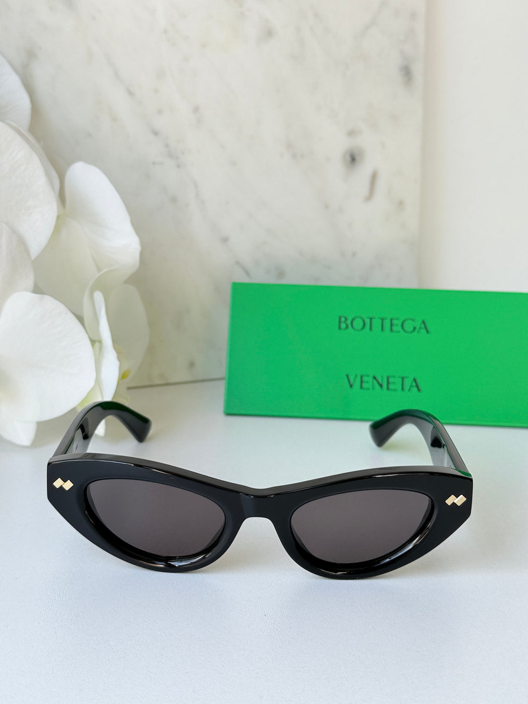 Black cat-eye sunglasses with dark lenses and gold-tone emblems on the temples.