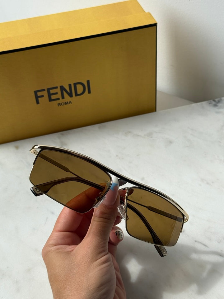 Fendi metal sunglasses held in hand, gold frame with brown lenses