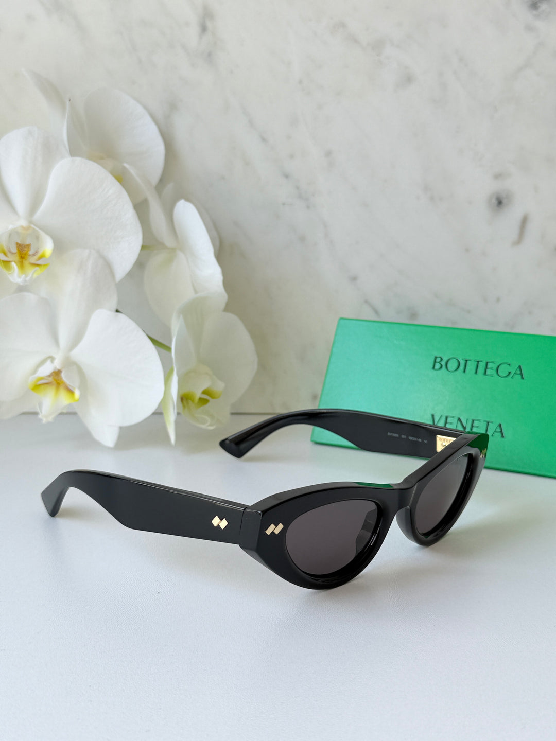 Black cat-eye sunglasses with dark lenses and gold-tone logo on the side arms.