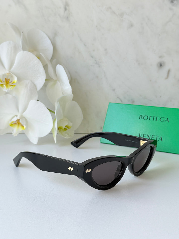 Black cat-eye sunglasses with dark lenses and gold-tone logo on the side arms.
