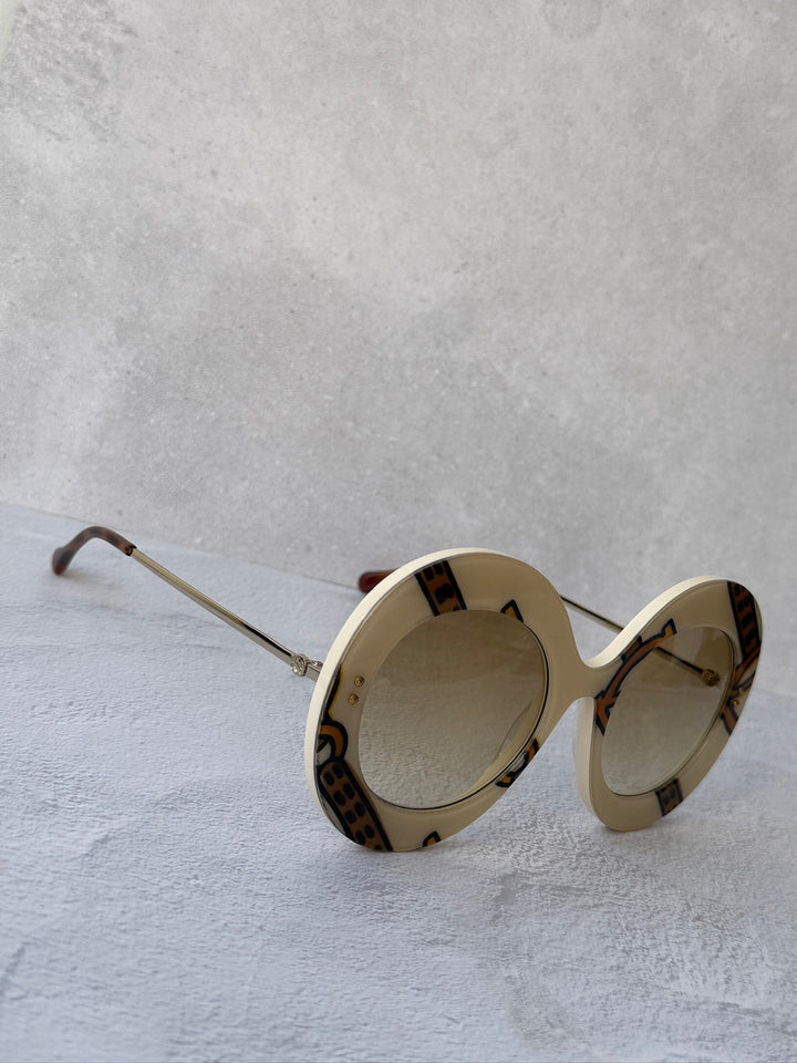 Cream round sunglasses with brown lenses, gold bridge, and patterned trim.