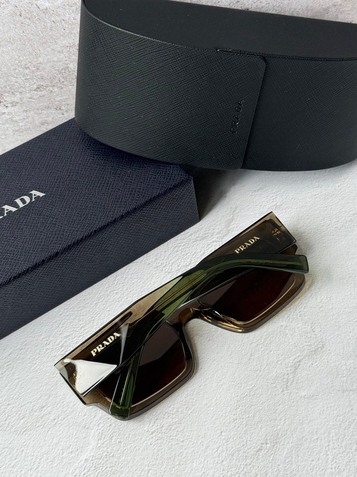 Prada sunglasses with transparent brown frames and brown lenses beside navy case