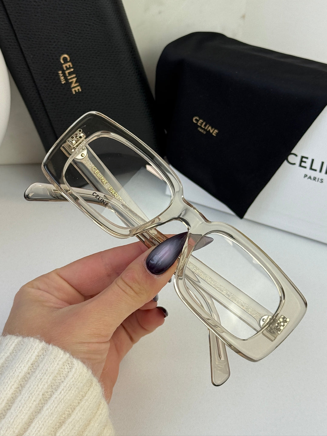 Celine eyeglass frames in translucent clear with gold-tone temples, held in hand