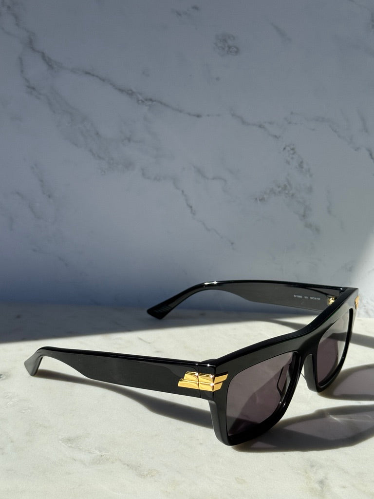 Black rectangular sunglasses with dark lenses, angled view with gold accents