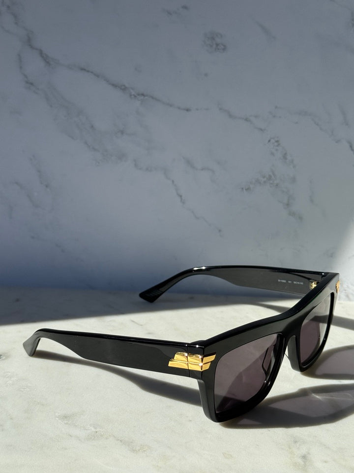 Black rectangular sunglasses with dark lenses, angled view with gold accents
