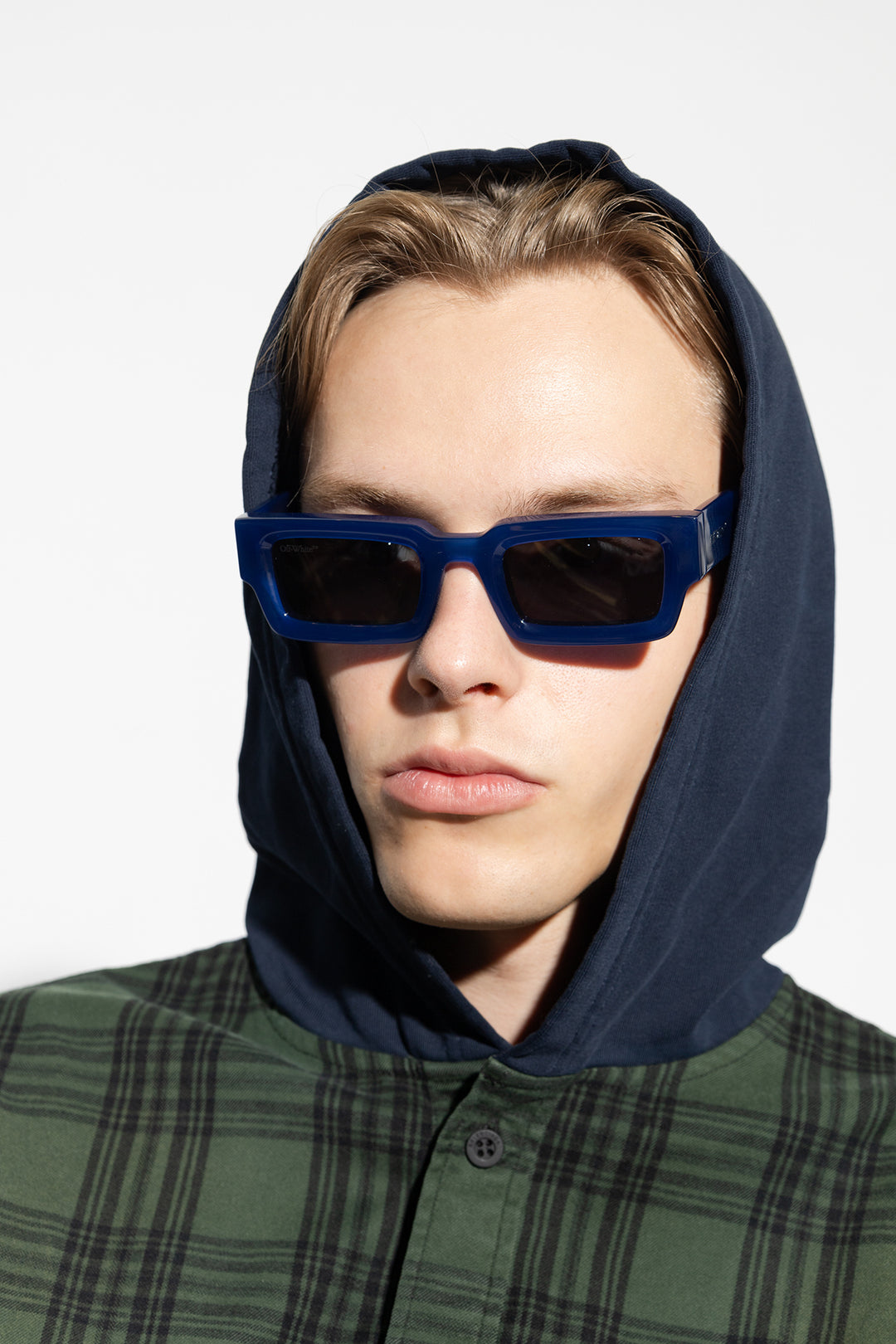 Blue square sunglasses with dark lenses on a hooded model.