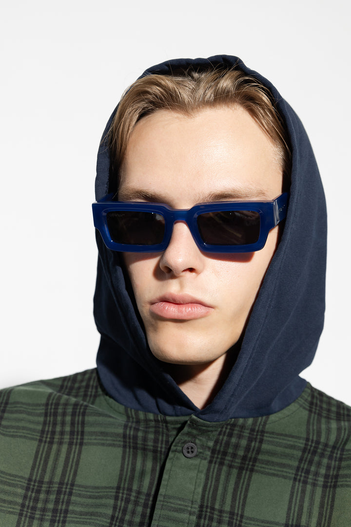 Blue square sunglasses with dark lenses on a hooded model.