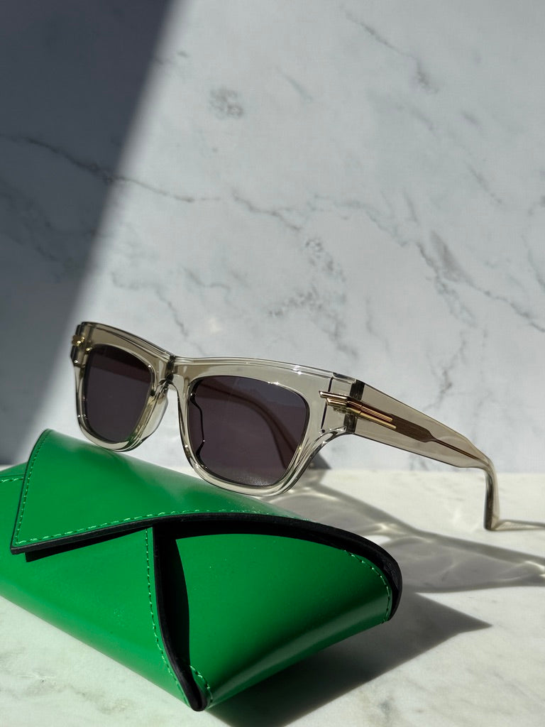 Mitre rectangular sunglasses with clear frame, dark lenses, resting on green pouch