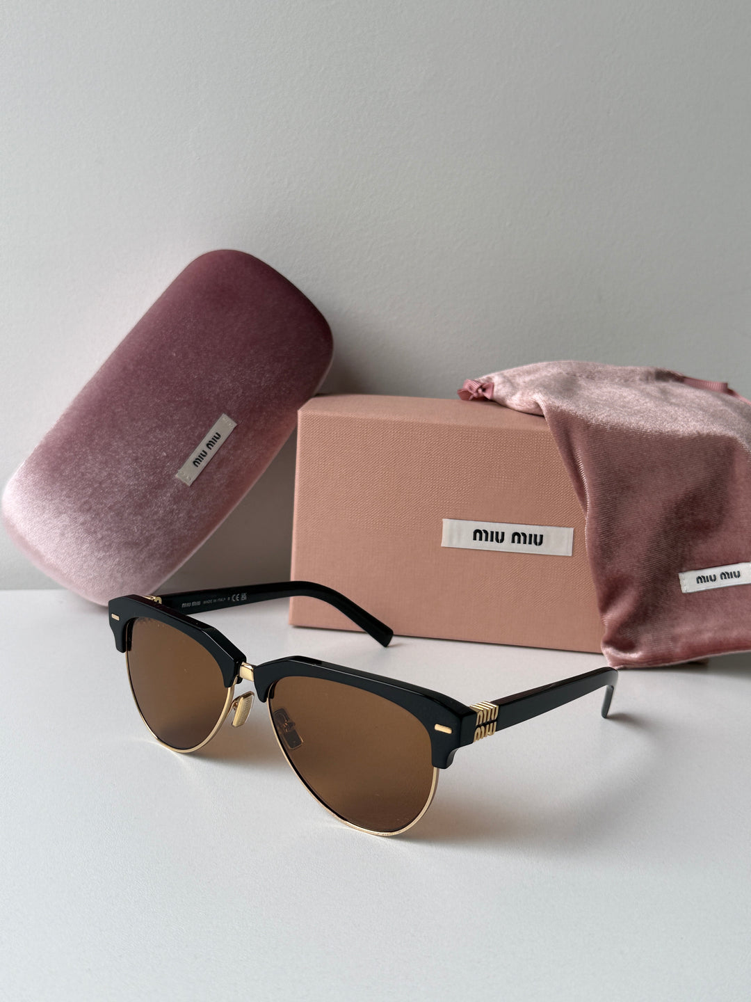 Miu Miu black cat-eye sunglasses with brown lenses beside dust bag and pink cloth