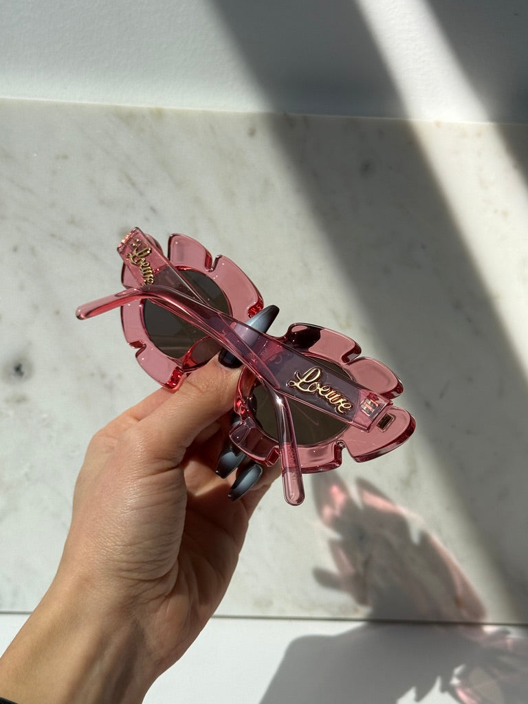 Loewe pink flower sunglasses held in hand, dark lenses and Loewe logo on temples