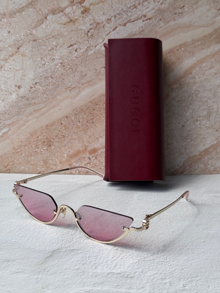 Gucci half-rim sunglasses with gold frame and pink lenses, folded on cloth