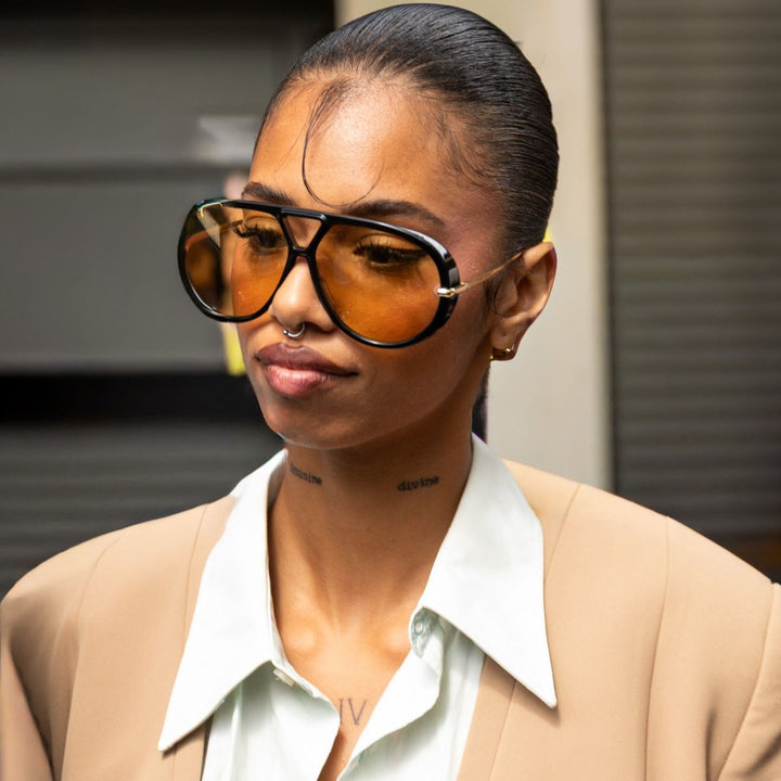 Black aviator sunglasses with amber lenses and gold drop earrings, side profile view.
