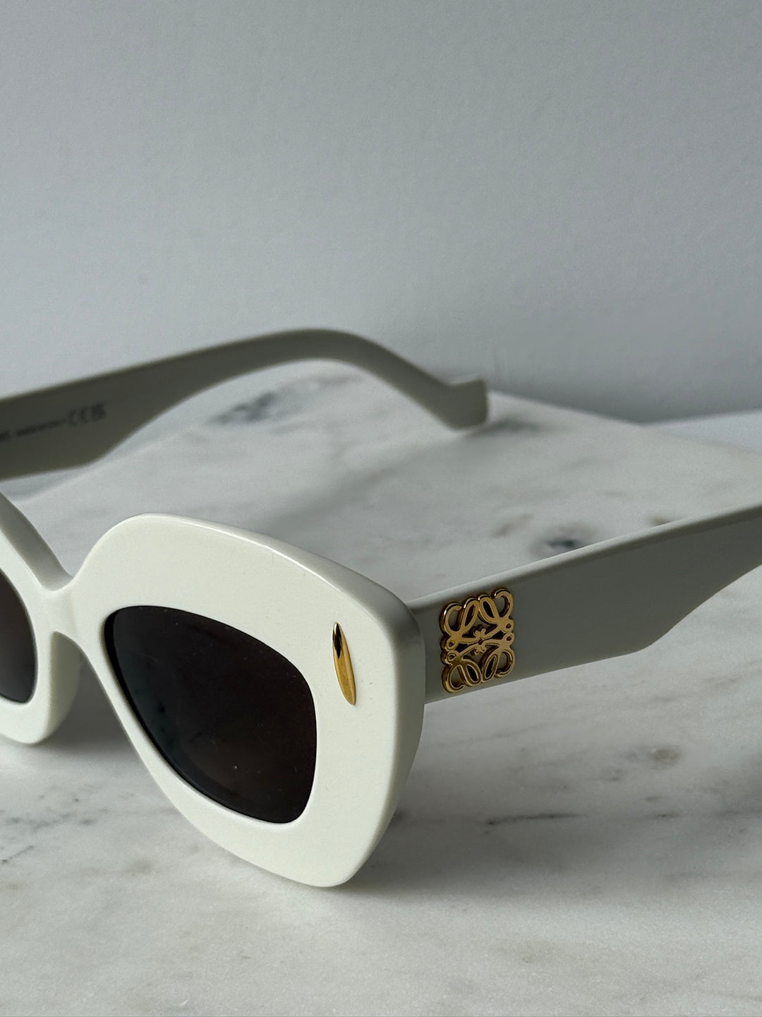White cat-eye sunglasses with dark lenses and gold logo on temple